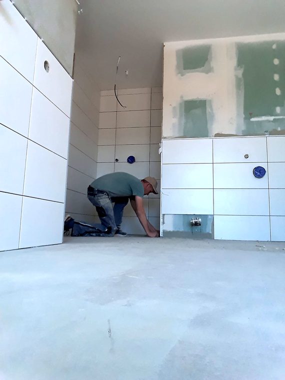 Fliesenleger bei der Arbeit im Bad, Wandfliesen bereits gesetzt
