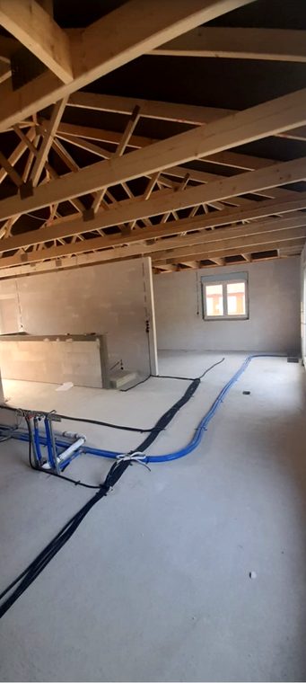 Dachgeschoss im Rohbau mit Leitungen auf dem Boden